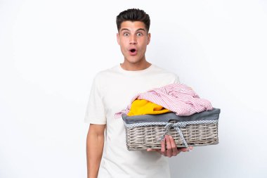 Çamaşır sepetini tutan beyaz arka planda yüzü şaşırmış genç beyaz bir adam.