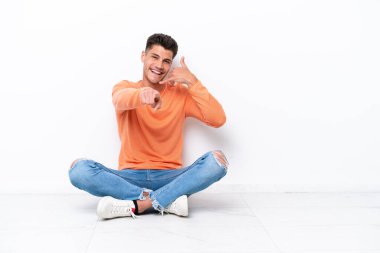 Genç adam beyaz arka planda izole bir şekilde yerde oturuyor.