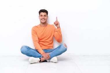 Beyaz arka planda izole bir şekilde yerde oturan genç adam işaret parmağıyla işaret etmek harika bir fikir.