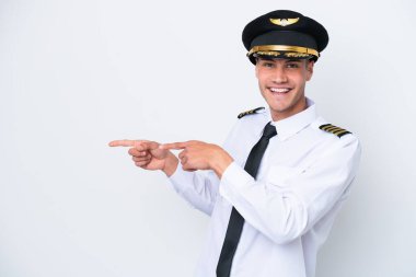 Kafkasyalı uçak pilotu beyaz arka planda izole edildi. Parmağını yana uzattı ve bir ürün sundu.