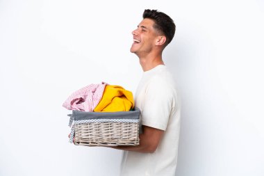Çamaşır sepetini tutan beyaz arka planda izole genç beyaz bir adam yan yana gülüyor.
