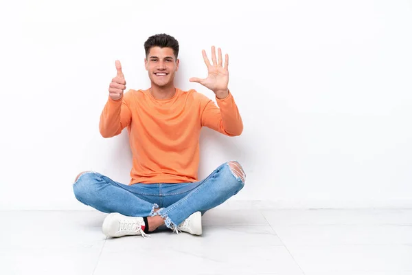 Young Man Sitting Floor Isolated White Background Counting Six Fingers — Zdjęcie stockowe