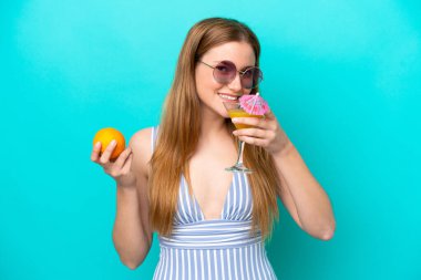 Mavi arka planda mayo giymiş ve elinde kokteyl tutan genç bir kadın.