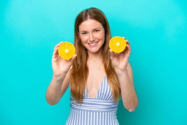 Mavi arka planda mayo giymiş ve elinde turuncu bir elbise tutan genç bir kadın.