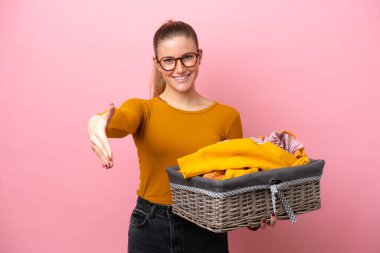 Pembe arka planda izole edilmiş çamaşır sepetini tutan beyaz bir kadın iyi bir anlaşma yaptığı için el sıkışıyor.