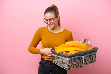 Pembe arka planda izole edilmiş çamaşır sepetini tutan beyaz bir kadın.