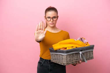 Pembe arka planda izole edilmiş çamaşır sepeti tutan beyaz bir kadın dur hareketi yapıyor.