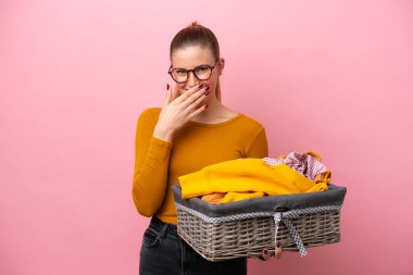 Pembe arka planda izole edilmiş çamaşır sepeti tutan beyaz bir kadın mutlu ve gülümseyen bir ağızla eli örtüyor.