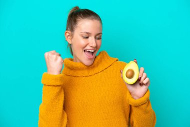 Mavi arka planda avakado tutan beyaz bir kadın zaferi kutluyor.
