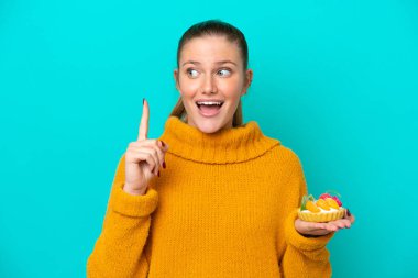 Mavi arka planda izole edilmiş turta tutan beyaz bir kadın çözümü fark etmek için parmağını kaldırıyor.