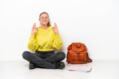 Beyaz arka planda Zen pozunda beyaz bir zeminde oturan beyaz tenli genç bayan.