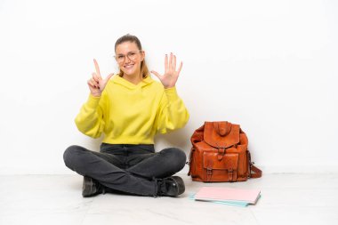 Beyaz arka planda bir katta oturan beyaz tenli genç bir kadın yediyi parmaklarıyla sayıyor.