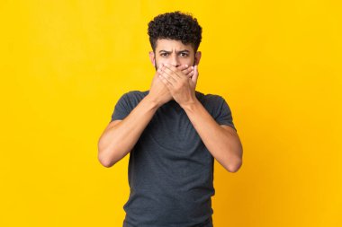 Sarı arka planda izole edilmiş genç Faslı adam elleriyle ağzını kapatıyor.