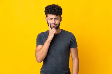 Genç Faslı adam sarı arka planda izole edilmiş ve düşünüyor.