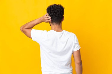 Genç Faslı adam sarı arka planda izole edilmiş ve düşünüyor.