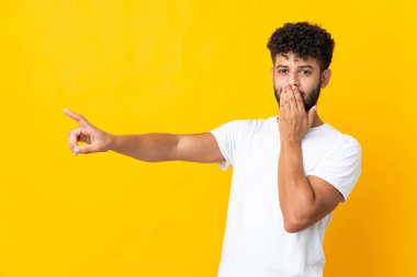 Faslı genç adam sarı arka planda izole edilmiş, sürpriz bir ifadeyle işaret ederken...