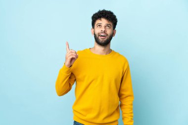 Faslı genç bir adam mavi arka planda izole edilmiş yukarı bakıyor ve şaşırıyor.