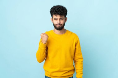 Faslı genç bir adam mutsuz bir ifadeyle mavi arka planda izole edilmiş.