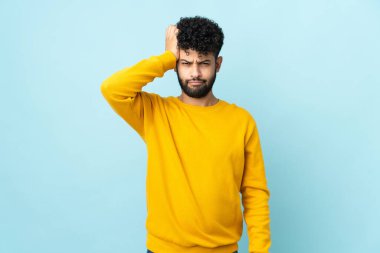 Faslı genç bir adam mavi arka planda hayal kırıklığıyla izole edilmiş ve anlamamış.
