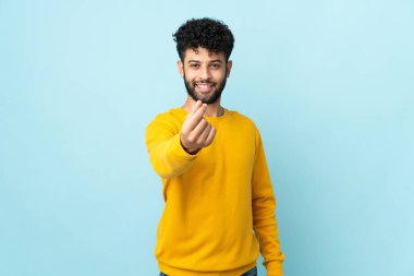 Faslı genç bir adam mavi arka planda izole edilmiş para hareketi yapıyor.