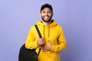 Spor çantalı genç Faslı adam mor arka planda izole edilmiş gülümsüyor.