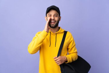 Spor çantalı genç Faslı adam mor arka planda izole edilmiş ağzı açık bağırıyor.