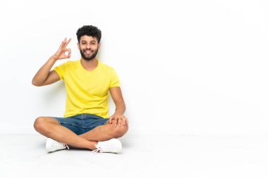 Genç Faslı yakışıklı adam izole bir zeminde oturuyor. Parmaklarıyla işaret veriyor.