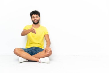 Genç Faslı yakışıklı adam izole bir zeminde oturuyor ve iyi bir anlaşma için el sıkışıyor.