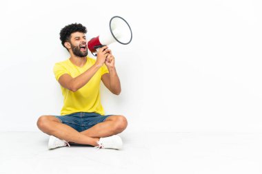Genç Faslı yakışıklı adam izole bir arka planda yerde oturmuş megafonla bağırıyor.
