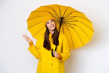 Young Brazilian woman with rainproof coat and umbrella isolated on white background extending hands to the side for inviting to come