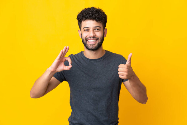 Young Moroccan man isolated on yellow background showing ok sign and thumb up gesture