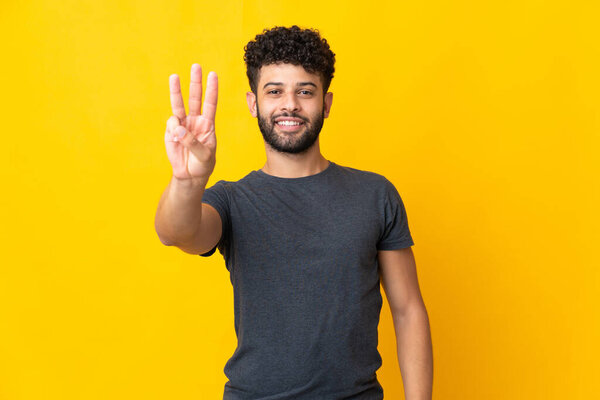 Young Moroccan man isolated on yellow background happy and counting three with fingers