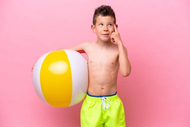 Pembe arka planda izole edilmiş bir plaj topu tutan beyaz bir çocuk. Şüpheleri var ve kafası karışmış bir yüz ifadesi var.