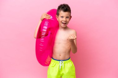 Küçük beyaz çocuk pembe arka planda izole edilmiş şişirilebilir bir çörek tutuyor. Kazanan pozisyonda zaferi kutluyor.