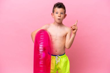 Küçük beyaz bir çocuk pembe arka planda izole edilmiş şişirilebilir bir çörek tutuyor. Çözümü bulmak için parmağını kaldırıyor.