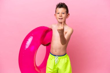 Küçük beyaz bir çocuk pembe arka planda izole edilmiş şişme bir çörek tutuyor.