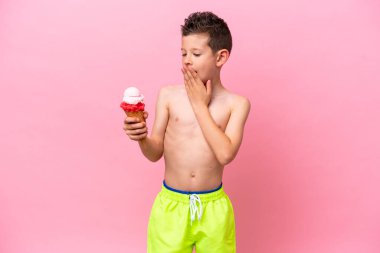 Pembe arka planda izole edilmiş, şaşırmış ve şok olmuş bir yüz ifadesiyle dondurma yiyen beyaz bir çocuk.