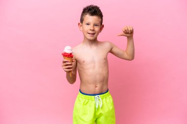 Küçük beyaz bir çocuk pembe arka planda izole edilmiş, gururlu ve kendini beğenmiş bir dondurma yiyor.