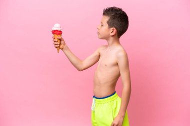 Küçük beyaz bir çocuk pembe arka planda izole edilmiş, mutlu bir ifadeyle dondurma yiyor.