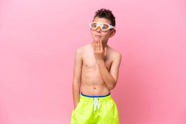 Pembe arka planda izole edilmiş dalış gözlüğü takan beyaz çocuk gülümserken yukarı bakıyor.