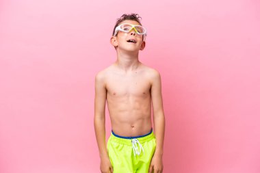 Pembe arka planda izole edilmiş dalış gözlüğü takan küçük beyaz çocuk gülüyor.