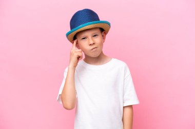 Pembe arka planda izole edilmiş şapka takan küçük beyaz bir çocuk. Şüpheleri var ve kafası karışmış bir yüz ifadesi var.