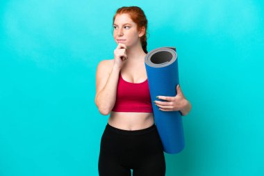 Genç spor kırmızısı kadın yoga derslerine giderken elinde mavi arka planda bir minder tutarken kuşkuları ve düşünceleri vardı.