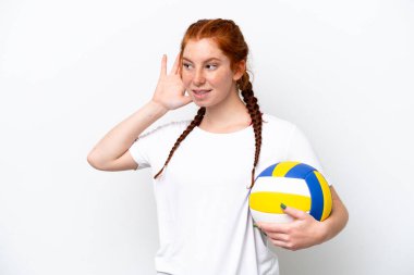 Beyaz arka planda izole edilmiş voleybol oynayan beyaz tenli genç bir kadın elini kulağına koyarak bir şeyler dinliyor.