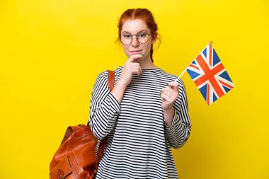 Young hispanic woman holding an United Kingdom flag isolated on yellow background thinking
