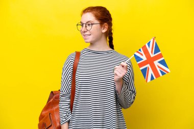 Young hispanic woman holding an United Kingdom flag isolated on yellow background looking side