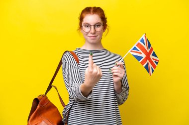 Young hispanic woman holding an United Kingdom flag isolated on yellow background doing coming gesture