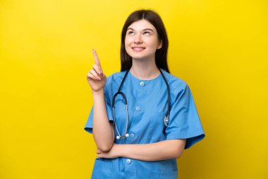 Sarı arka planda izole edilmiş genç cerrah doktor Rus kadın harika bir fikre işaret ediyor.