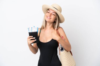 Mayo giymiş genç bir kadın beyaz arka planda izole edilmiş bir pasaport taşıyor. Başparmakları havada çünkü iyi bir şey oldu.