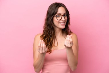 Pembe arka planda izole genç beyaz kadın para hareketi yapıyor.